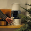 Aqualine waterfilter op houten aanrecht  met plant ervoor en arm met hand die water tapt
